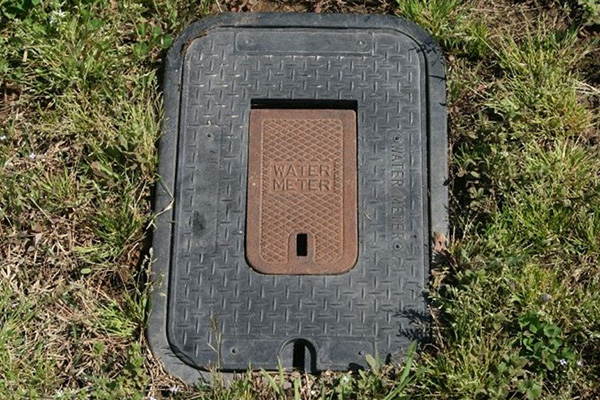 A concrete enclosure for a water meter in the ground surrounded by grass.