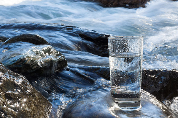 A glass of water sits on a rocky area of a river.