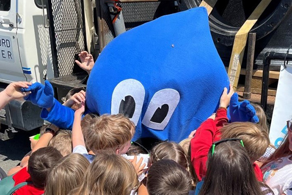 A water mascot greeting kids.