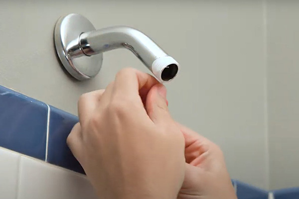 A person applying plumbers tape to install a new efficient showerhead