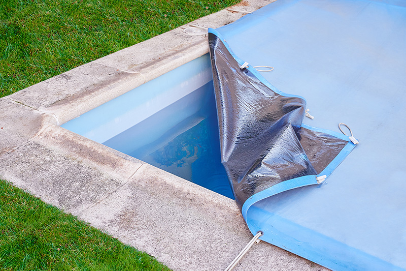 A pool with part of a cover pulled back exposing the water underneath, surrounded by grass.