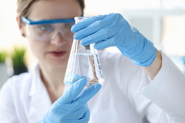 Woman scientist holding flask with transparent liquid in her hands closeup.